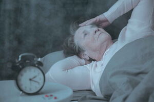 Eine Frau liegt im Bett. Auf dem Nachttisch steht ein Wecker. Es ist kurz vor halb drei in der Nacht. Sie fasst sich an den Kopf und kann nicht schlafen. Schlafstörungen können mit Hypnose effektiv überwunden werden.